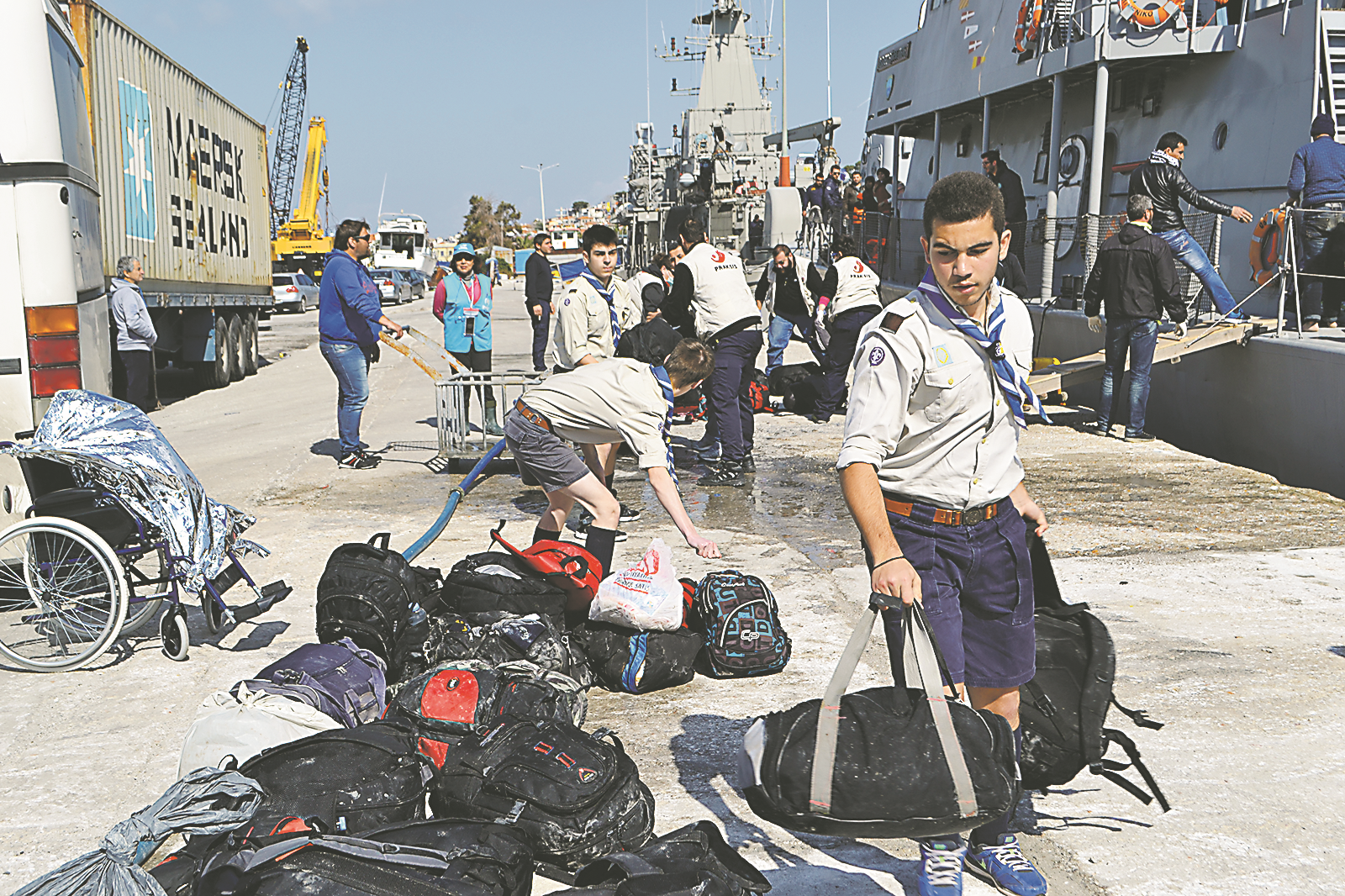 Μέλη του 3ου Σώματος προσκόπων του νησιού, μεταξύ των οποίων οι Γιάννης Σβώρος και Ξενοφών Κουκούτας βοηθούν στη μεταφορά σακιδίων των προσφύγων που μόλις έχουν φθάσει στο λιμάνι της Μυτιλήνης