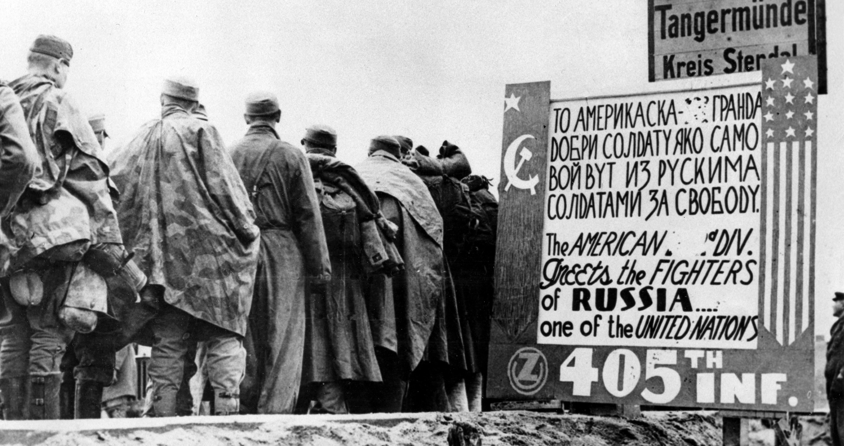 Συλληφθέντες Γερμανοί στρατιώτες περνούν μια ρωσοαγγλική πινακίδα που χτίστηκε από τους άνδρες του ένατου στρατού των ΗΠΑ στις 9 Μαΐου 1945. Η πινακίδα φέρει αριστερά την σημαία της ΕΣΣΔ  και δεξιά την αστερόεσσα σηματοδοτώντας την ένωση των συμμαχικών δυνάμεων κατά του φασισμού